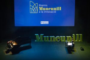 Teatro Principal. Letras en verde con la palabra MUNCUNILLO. Marco Mezquida tocando el piano y dos ingenieros en una mesa con la máquina de inteligencia artificial.